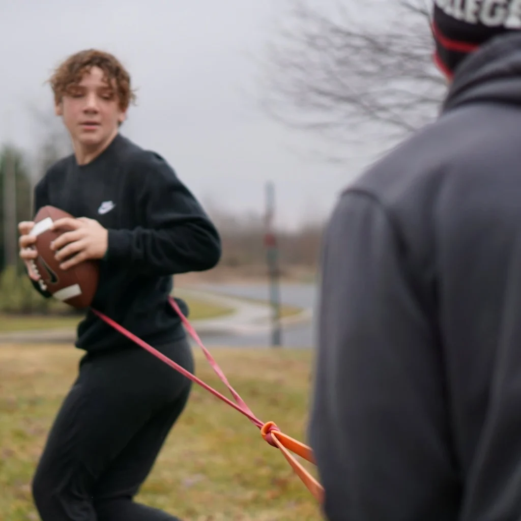 Peak Performance coach assisting athlete through banded football drill
